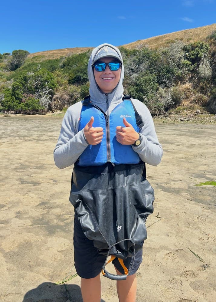 Nathan on the beach in a life vest and spray skirt, giving two thumbs up